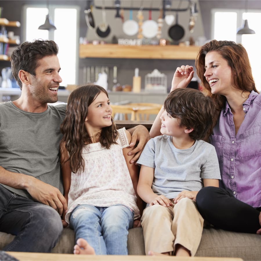 Family of 4 on the couch laughing and smiling together.